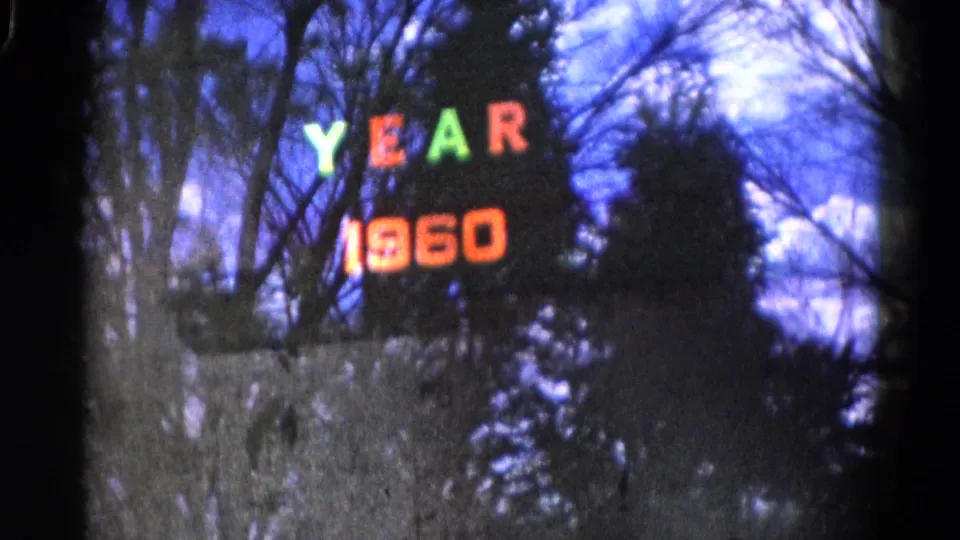 Final 1961 Wauconda frame showing the reflected YEAR 1960 sign beside dark trees and a cool sky.