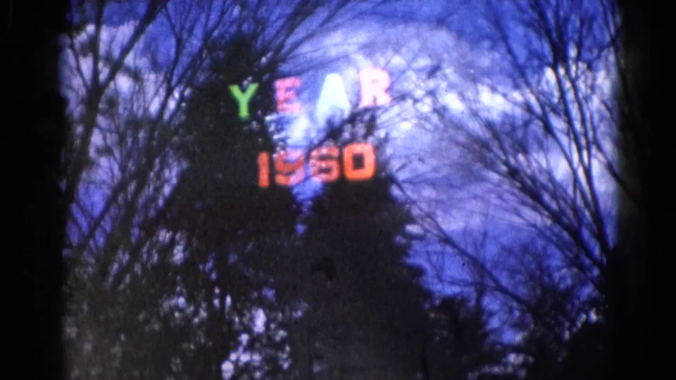 Wauconda, Illinois 8mm still showing a holiday "YEAR 1960" display in color, partly blocked by winter trees and film darkness.