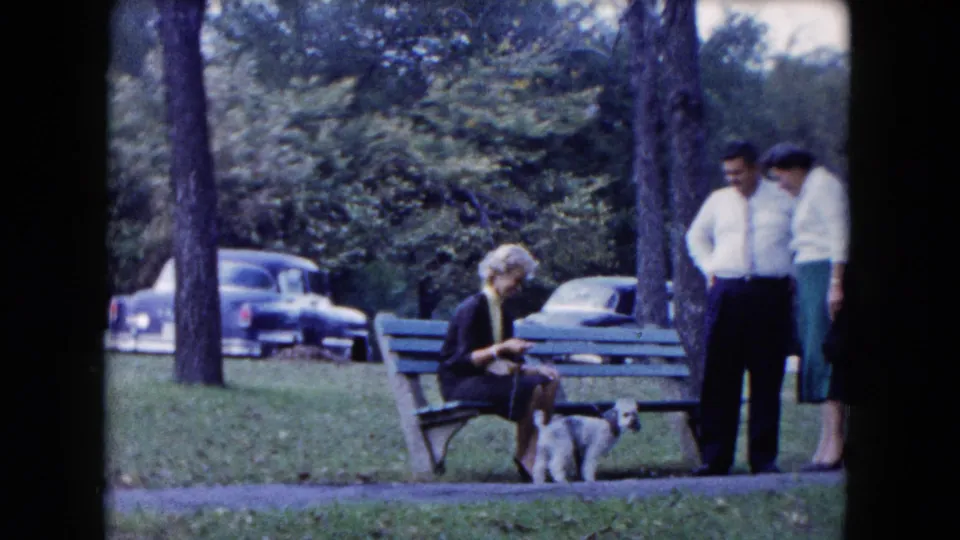 In a South Carolina park setting from the stated 1961 footage, a woman sits with a small leashed dog while two adults stand beside the bench.