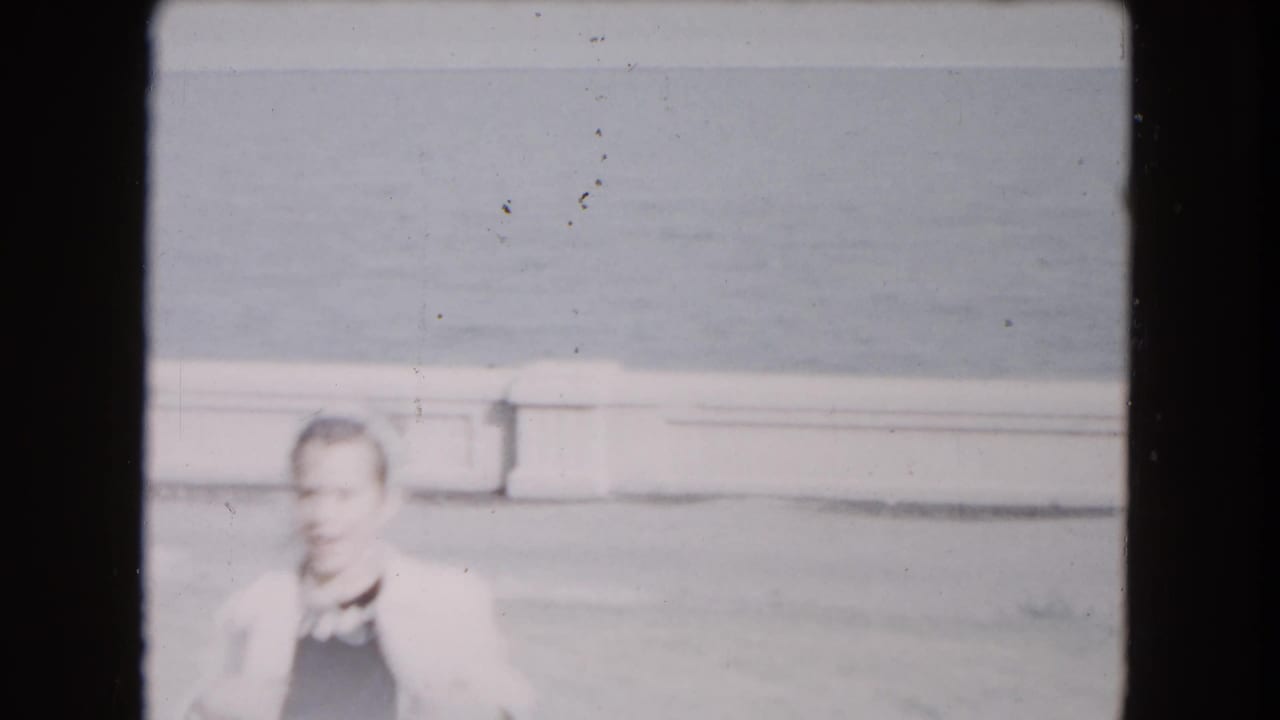 Adult man in a light jacket standing near a pond edge.