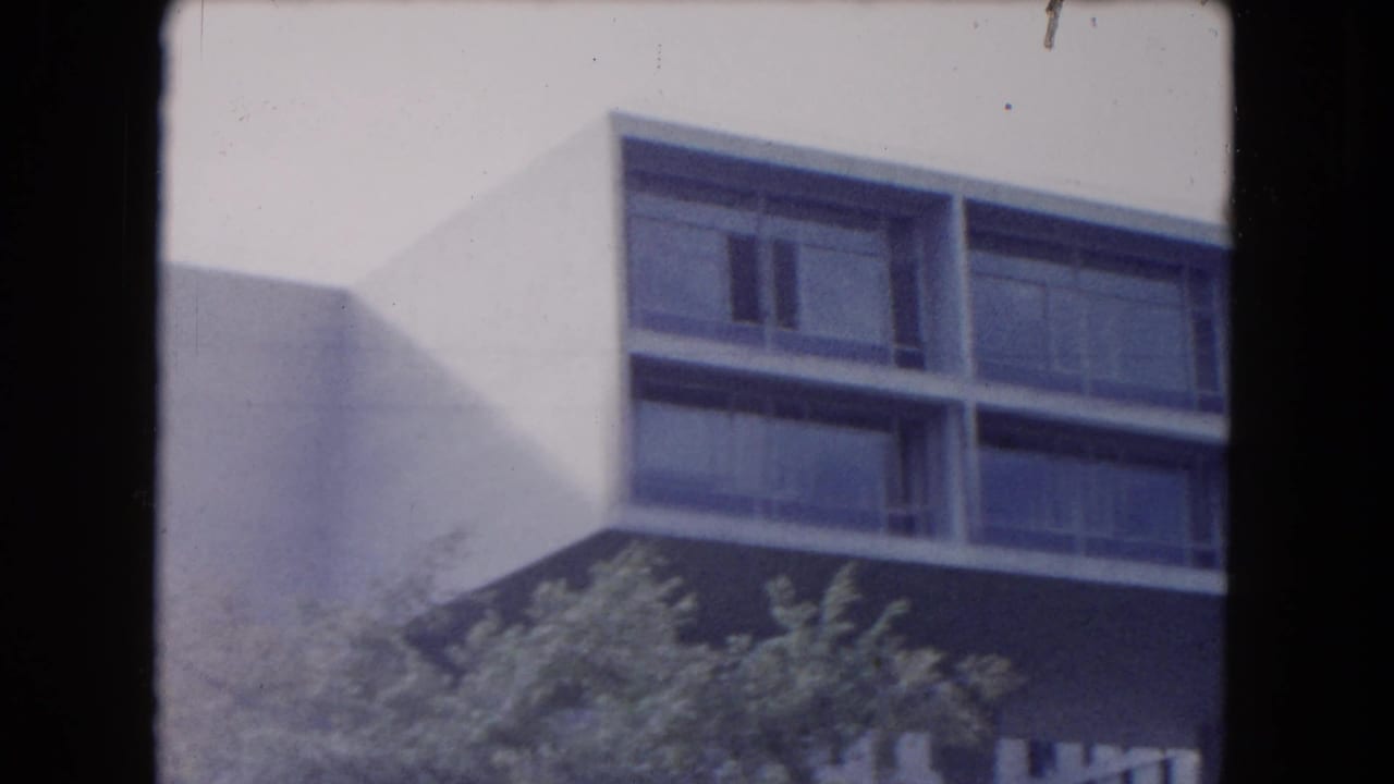 Upper corner of a modernist apartment building with long windows under a gray sky.