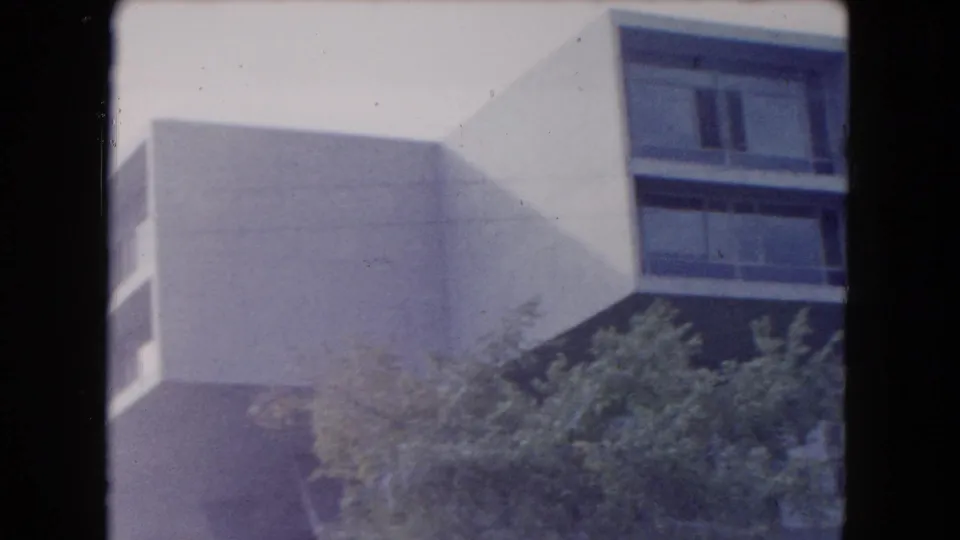 1961 South Carolina 8mm frame showing a white mid-century modern building exterior with cantilevered massing, dark window bands, and trees below.