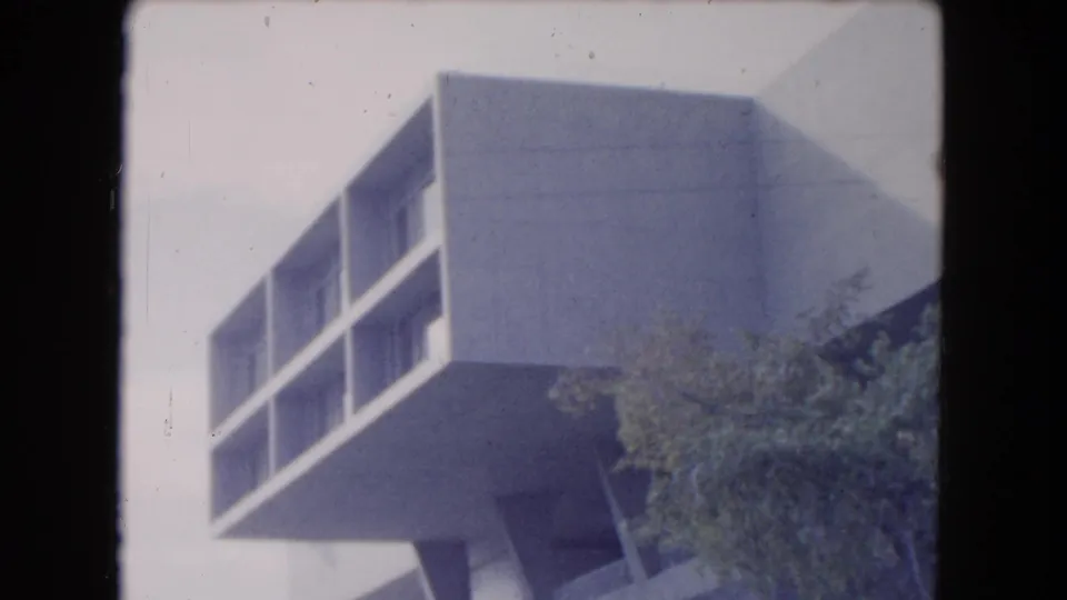 1961 South Carolina frame of a stark white modern building corner with recessed windows and a projecting upper volume above trees.