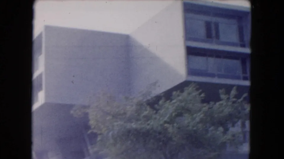 1961 South Carolina frame showing a white geometric building exterior, dark window band, leafy trees, and soft 8mm exposure.