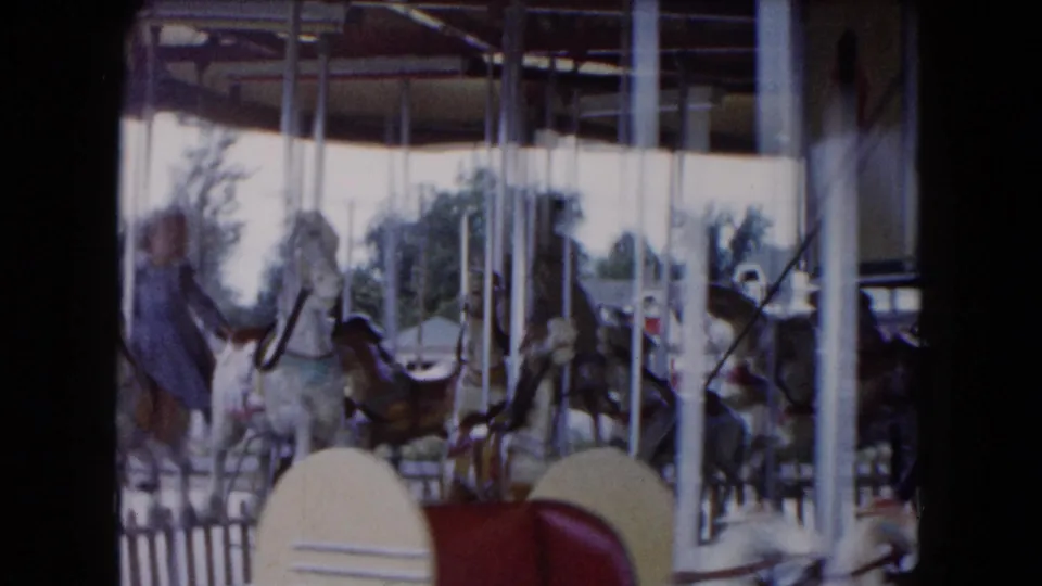 1961 South Carolina 8mm frame showing painted carousel horses, vertical poles, and riders under a fairground ride canopy.