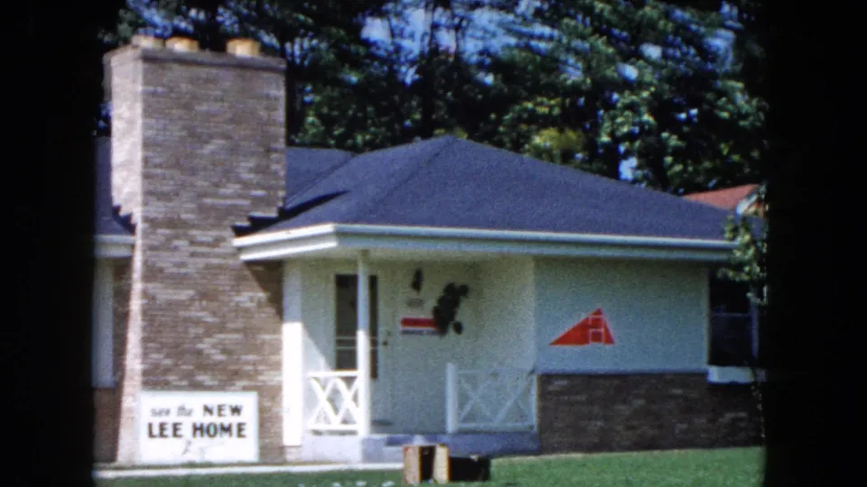 1961 South Carolina frame centered on a brick chimney, front entrance, lawn, and readable sign saying see the NEW LEE HOME.