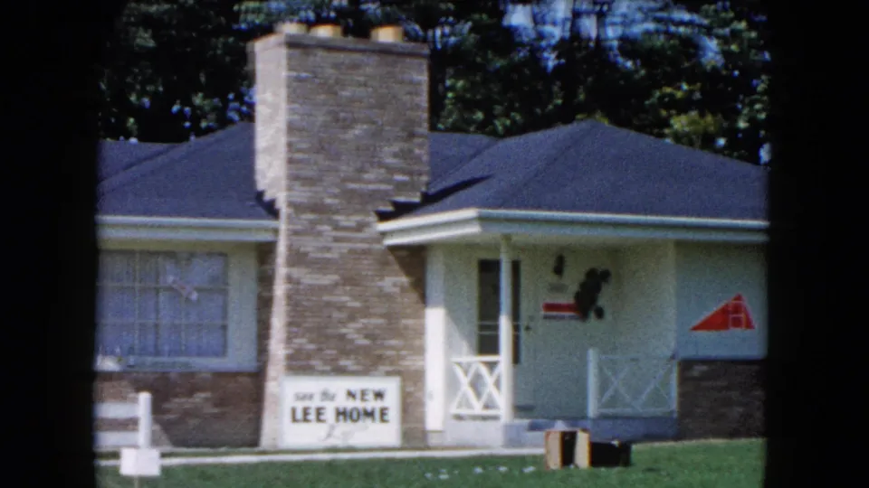 1961 South Carolina home-movie frame showing the house facade, central brick chimney, large window, porch railing, and Lee Home sign.