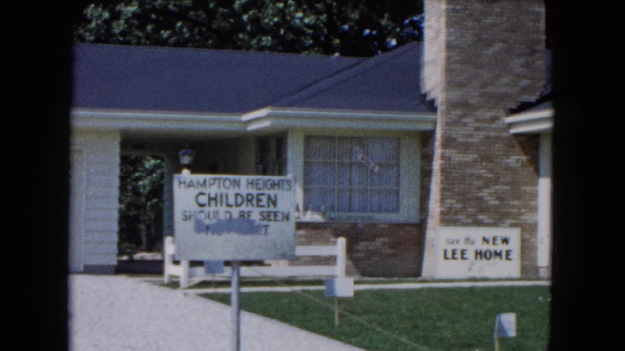 Suburban house with lawn signs, brick chimney, driveway, and dark film-frame borders.