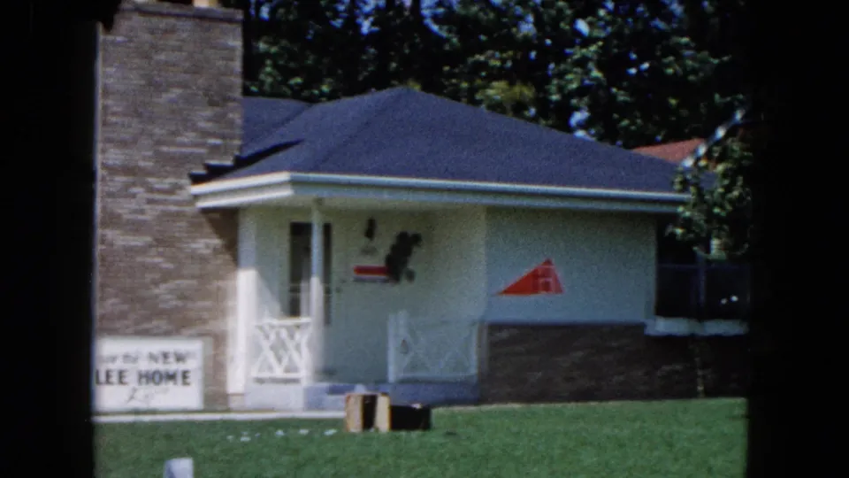 1961 South Carolina frame showing the right side of the house with porch, chimney, lawn, and a red triangular symbol on the wall.