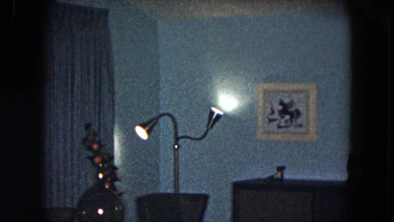 Dim room corner with blue curtains, a glowing two-headed floor lamp, framed wall print, and dark furniture.