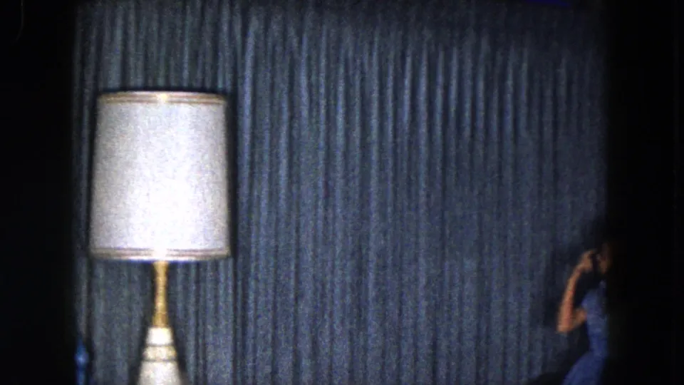 1961 South Carolina home interior with blue textured curtains, a white-shaded table lamp, and a partially visible person along the right side.
