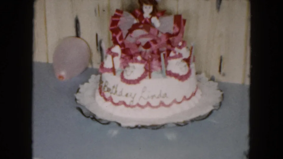 Final frame shows the decorated Birthday Linda cake with pink balloon, candles, doll topper, and scalloped serving plate in a private South Carolina interior.