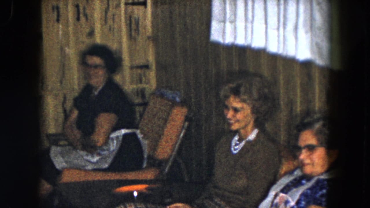 Three older women sit in lounge chairs beside wood-paneled walls and a curtained window.