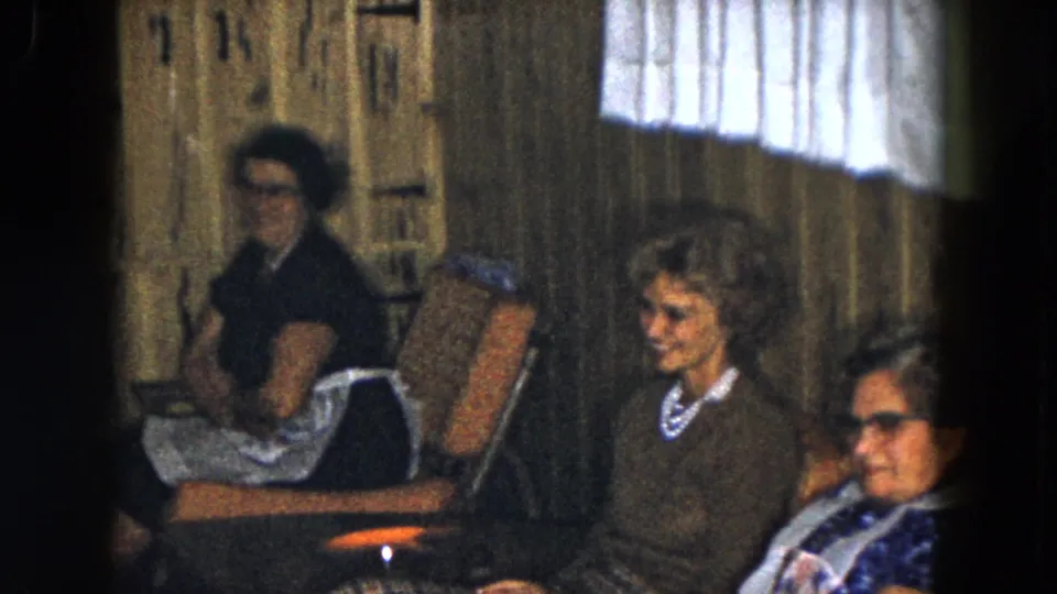 In a 1961 South Carolina home-movie frame, three older women sit in a wood-paneled lounge or community room.