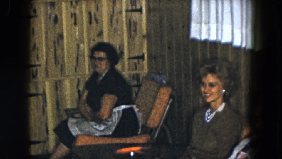 A 1961 South Carolina home-movie frame shows older women seated in a paneled lounge, with one figure partly cropped at right.