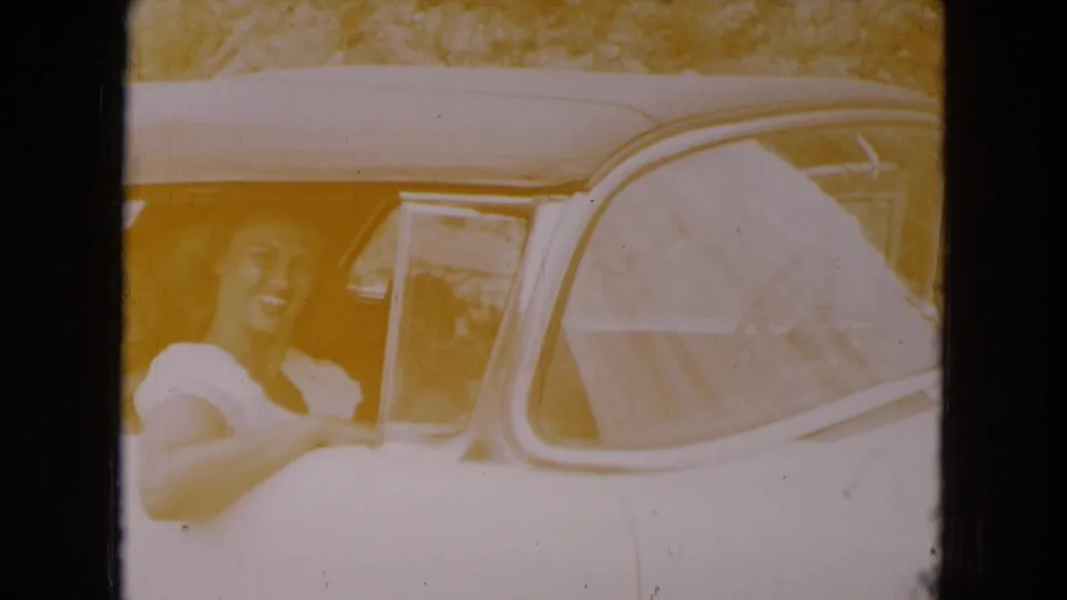 Faded 1961 South Carolina 8mm frame showing a smiling woman beside the passenger window of a white convertible.