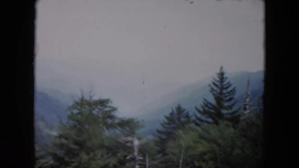 1961 South Carolina 8mm frame showing hazy mountain ridges and evergreen trees through dark window-like edges.