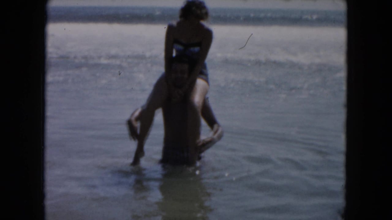 Man carries woman on his shoulders in shallow ocean water.