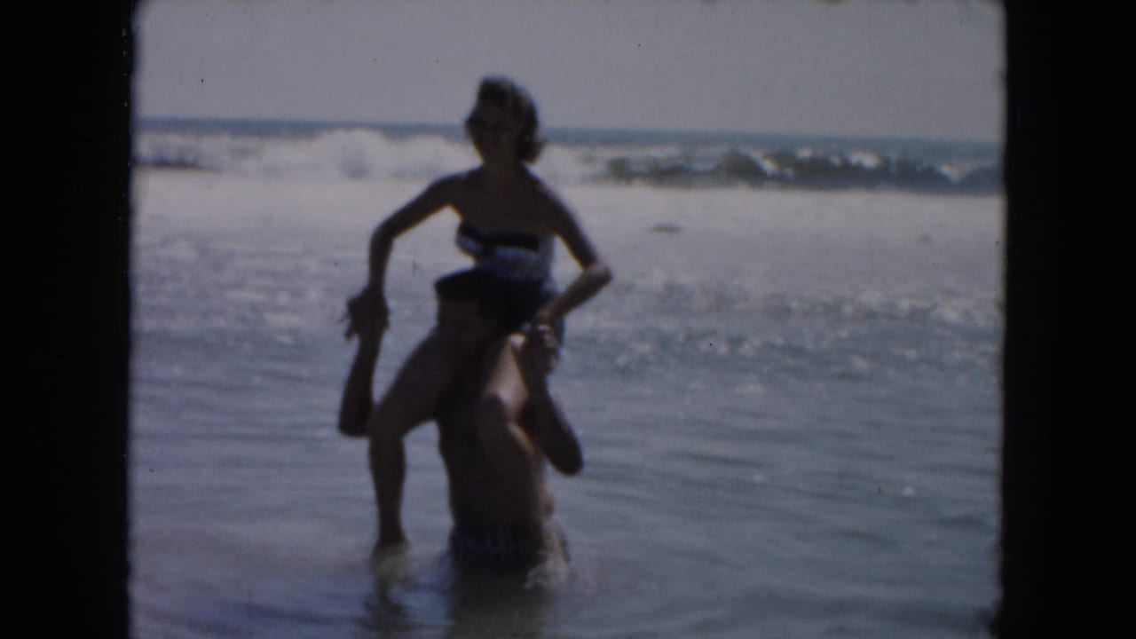 A woman in a dark swimsuit balances on a man's shoulders in shallow South Carolina surf, supported by 1961 metadata.