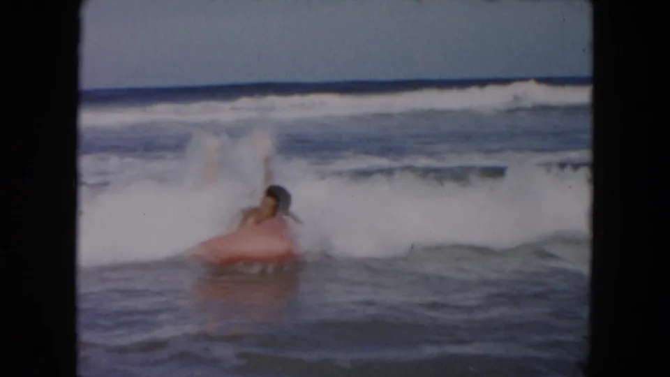 In the South Carolina beach home movie, the man lies low on the pink inflatable float while white surf rises behind him.