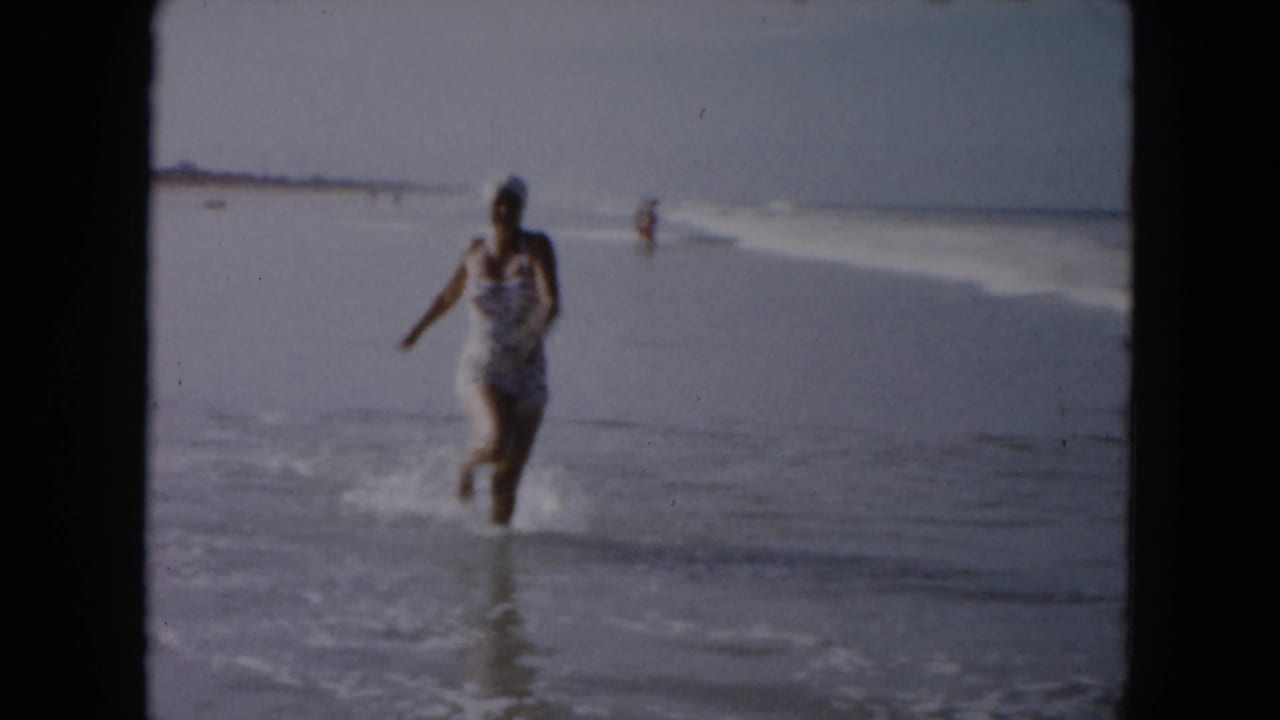 Woman in a patterned swimsuit runs through shallow ocean surf.