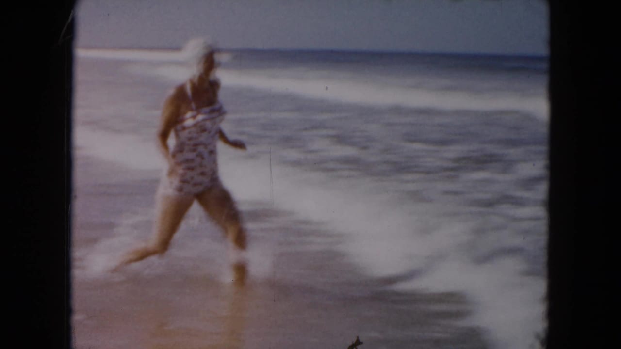 A woman in a patterned swimsuit and swim cap runs along the South Carolina shoreline as small waves break beside her.
