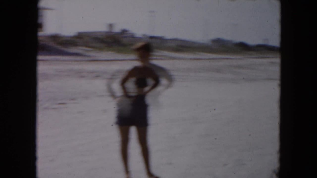 1961 South Carolina beach frame showing a person in dark swim trunks standing near shallow surf on wet sand.