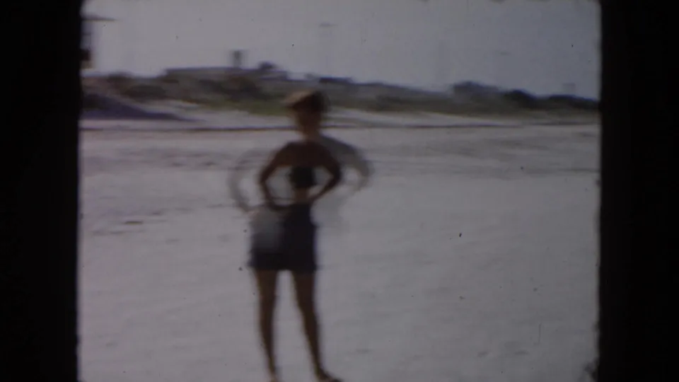 1961 South Carolina beach frame showing a person in dark swim trunks standing near shallow surf on wet sand.