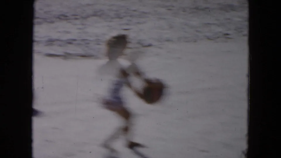 Motion-blurred 1961 South Carolina 8mm frame of a beachgoer crossing the sand with a ball near the shoreline.