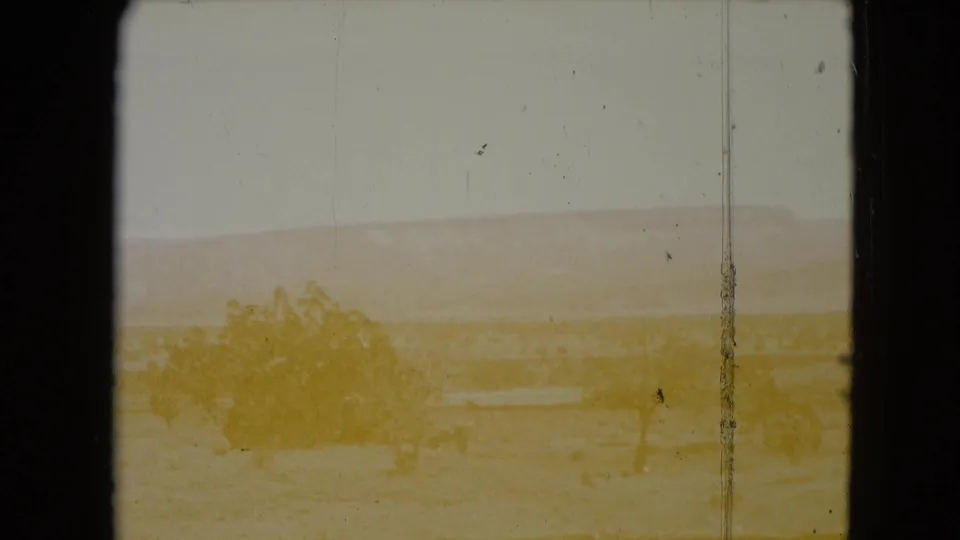 End frame of 1961 Nevada desert footage with severe color fading, pale mountain forms, shrubs, scratches, and yellowed exposure.