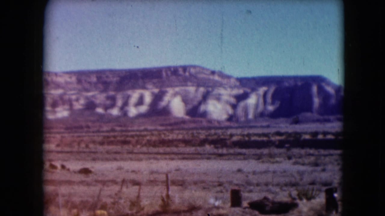 Dry desert foreground with wooden posts and a pale rocky ridge under blue sky.