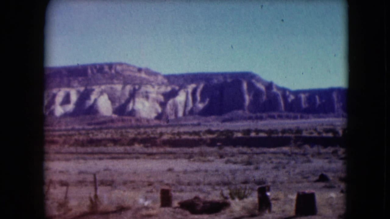 1961 Nevada 8mm frame with arid flats, scattered shrubs, wooden posts, and pale cliff-like rock formations.