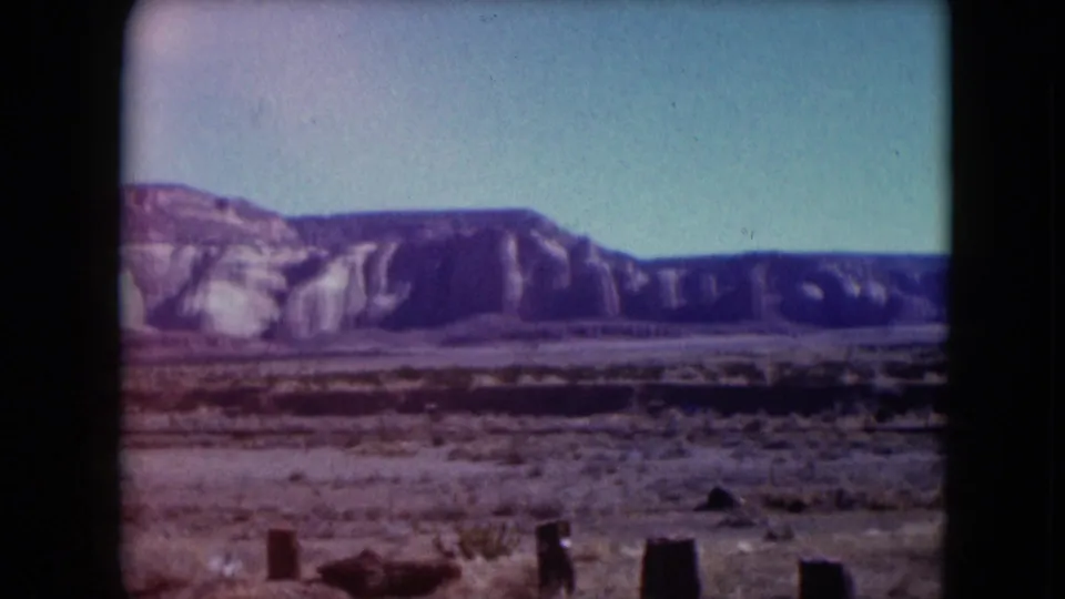 1961 Nevada 8mm frame showing a dry plain with scattered vegetation, fence or roadside posts, and a dark rocky ridge.