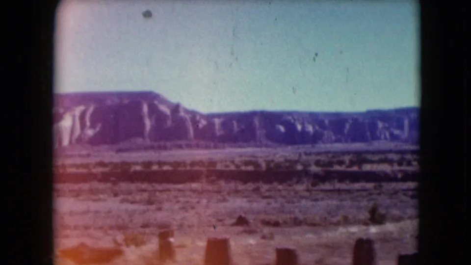 1961 Nevada 8mm frame with faded color, desert scrub, wooden posts, and a long ridge across the horizon.