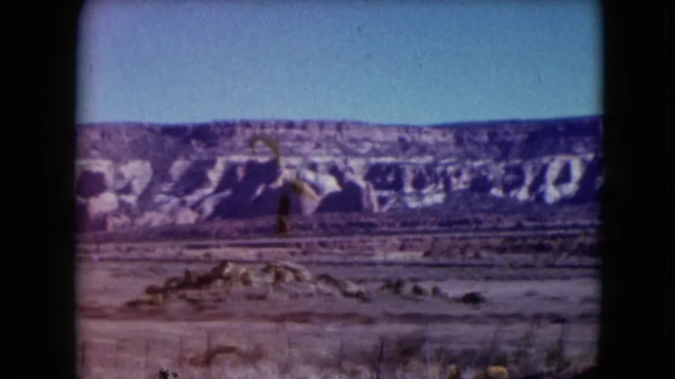1961 Nevada home-movie still with a panoramic mesa view, open desert ground, scattered vegetation, and visible 8mm gate edges.