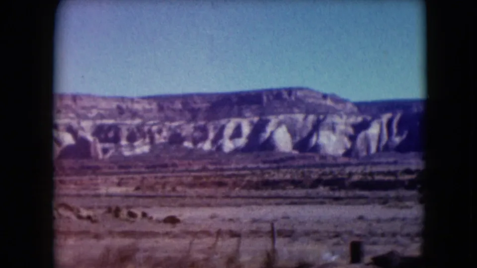 1961 Nevada 8mm still showing the mesa continuing across the horizon with scrubby desert foreground, fence elements, and dark rounded frame edges.