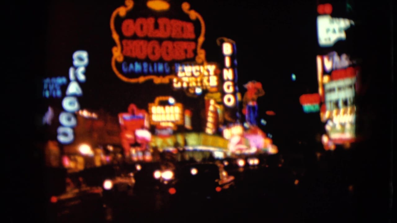 1961 Nevada home-movie view of Las Vegas neon signs, including the Golden Nugget area, with traffic lights and cars below.
