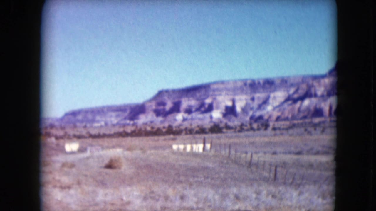Desert road or open ground with fence posts and low hills in the distance.