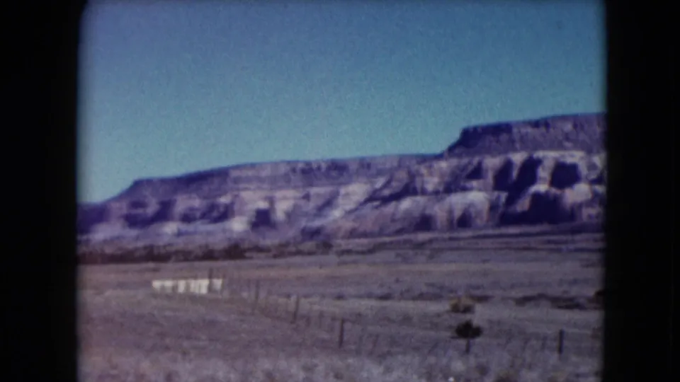 Nevada desert landscape from 1961 home-movie footage, showing fence posts, flat open land, and layered rocky hills.