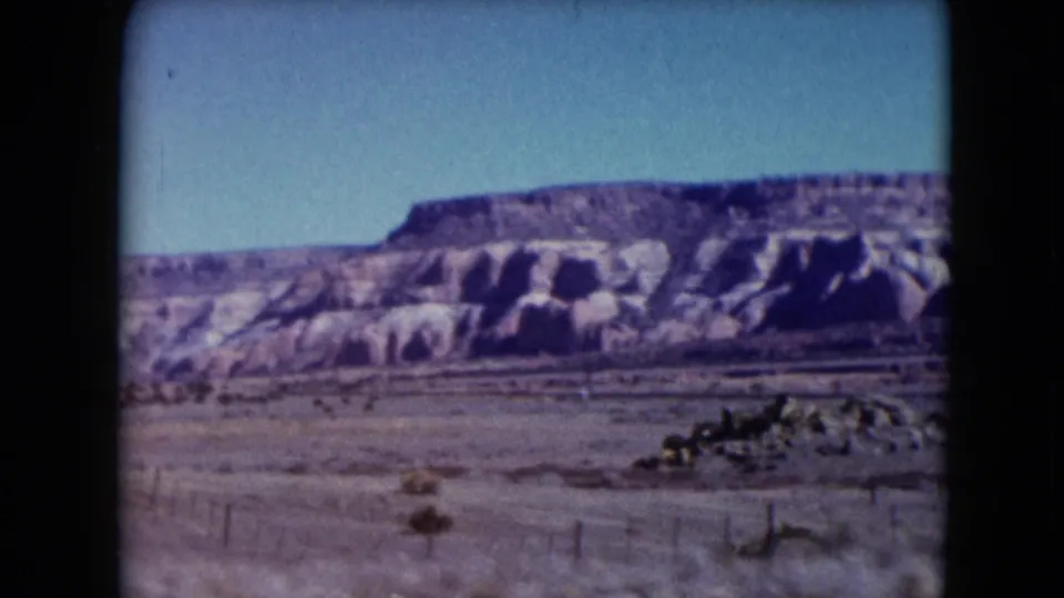 1961 Nevada desert view with rocky hills, scattered fence posts, scrub, and a low pile of stones in the foreground.