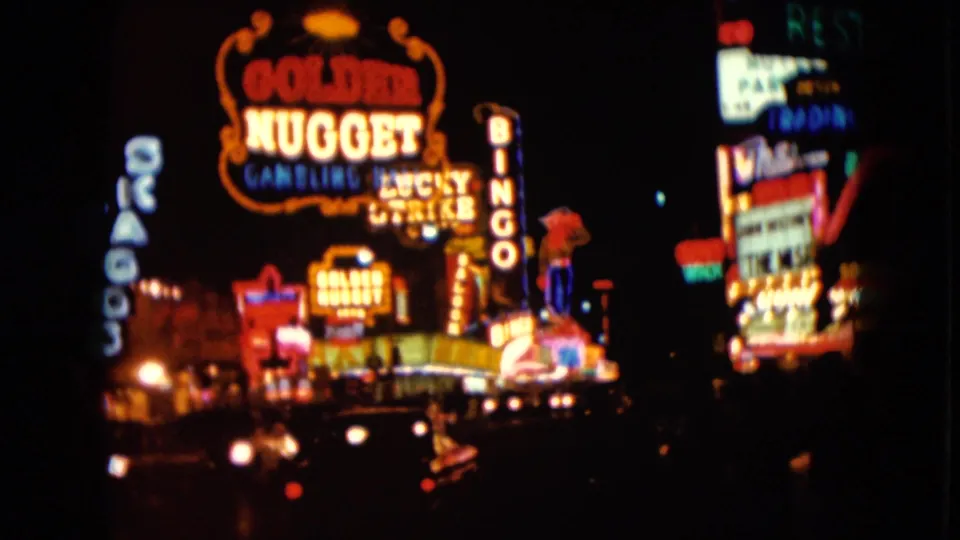 1961 Nevada night frame showing Golden Nugget neon, nearby casino signage, and headlights on a dark street.