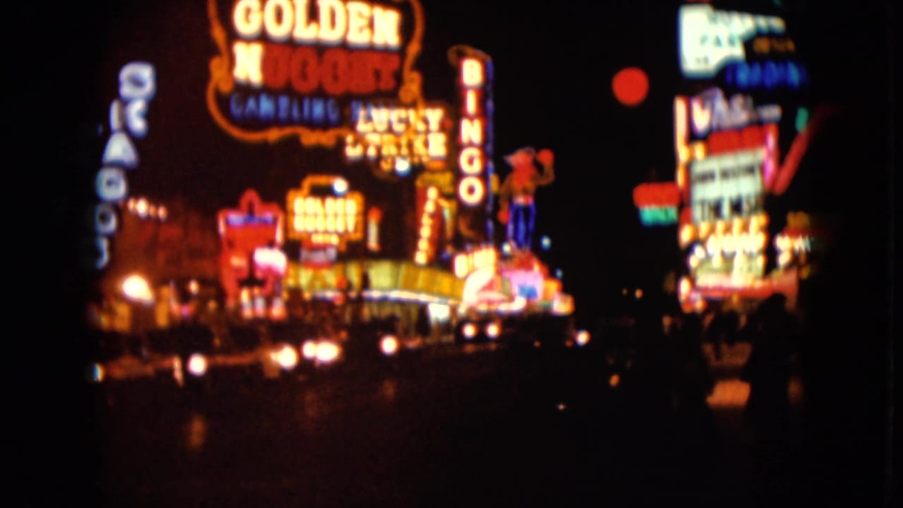 Blurred neon casino signs and car headlights on a dark street at night.