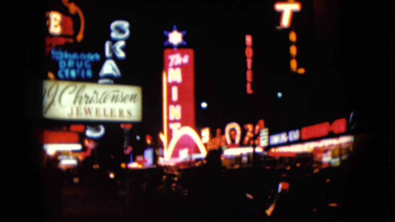 Blurred neon casino and storefront signs along a dark downtown street.