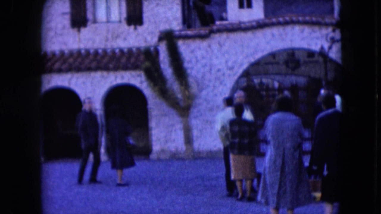 1961 Nevada home-movie frame showing adults gathered outside a historic-style stone building with arches and tiled roof details.