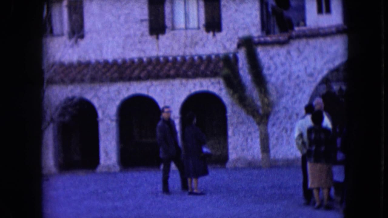 Two adults walk near three arched openings as another small group stands at the right edge.