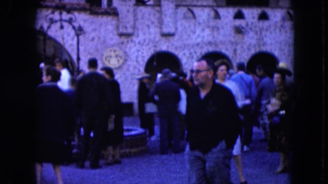 1961 Nevada home-movie frame showing adults in suits, coats, and dresses near a stone facade with arched doorways.