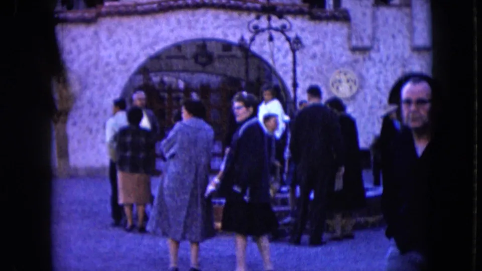 1961 Nevada crowd scene with adults in period coats and dresses gathered by an arched stone entrance.