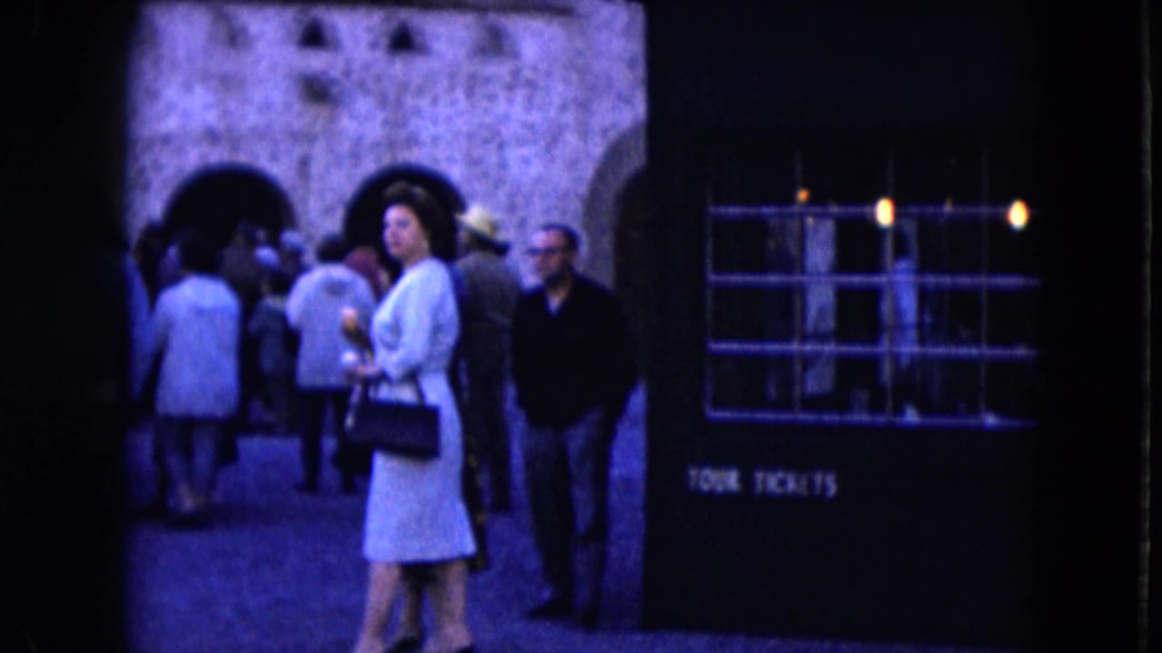1961 Nevada home-movie frame showing visitors near arched stone walls and a booth labeled TOUR TICKETS.