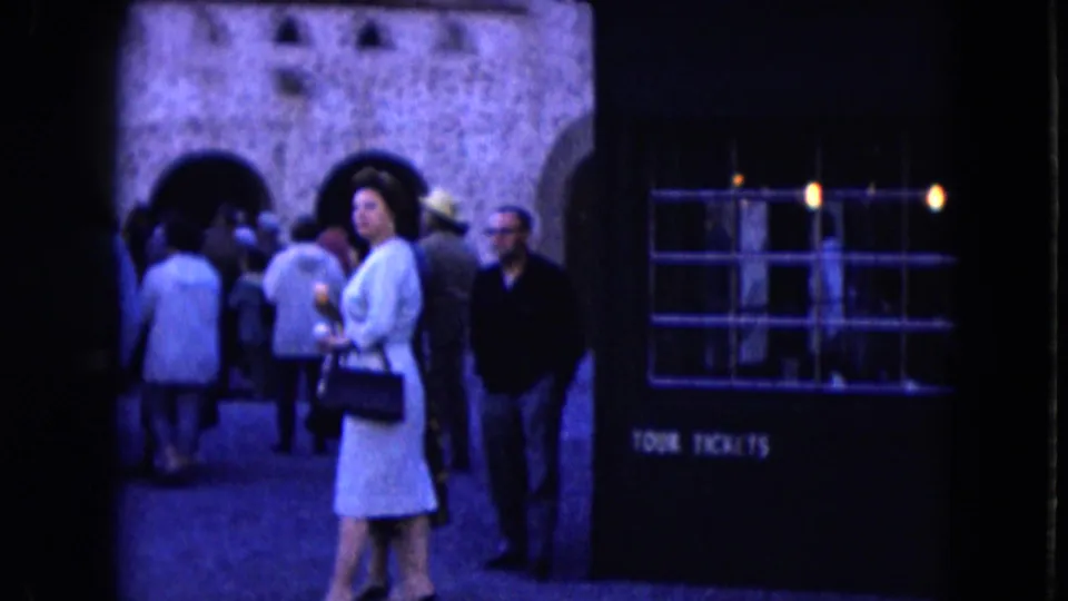1961 Nevada home-movie frame showing visitors near arched stone walls and a booth labeled TOUR TICKETS.