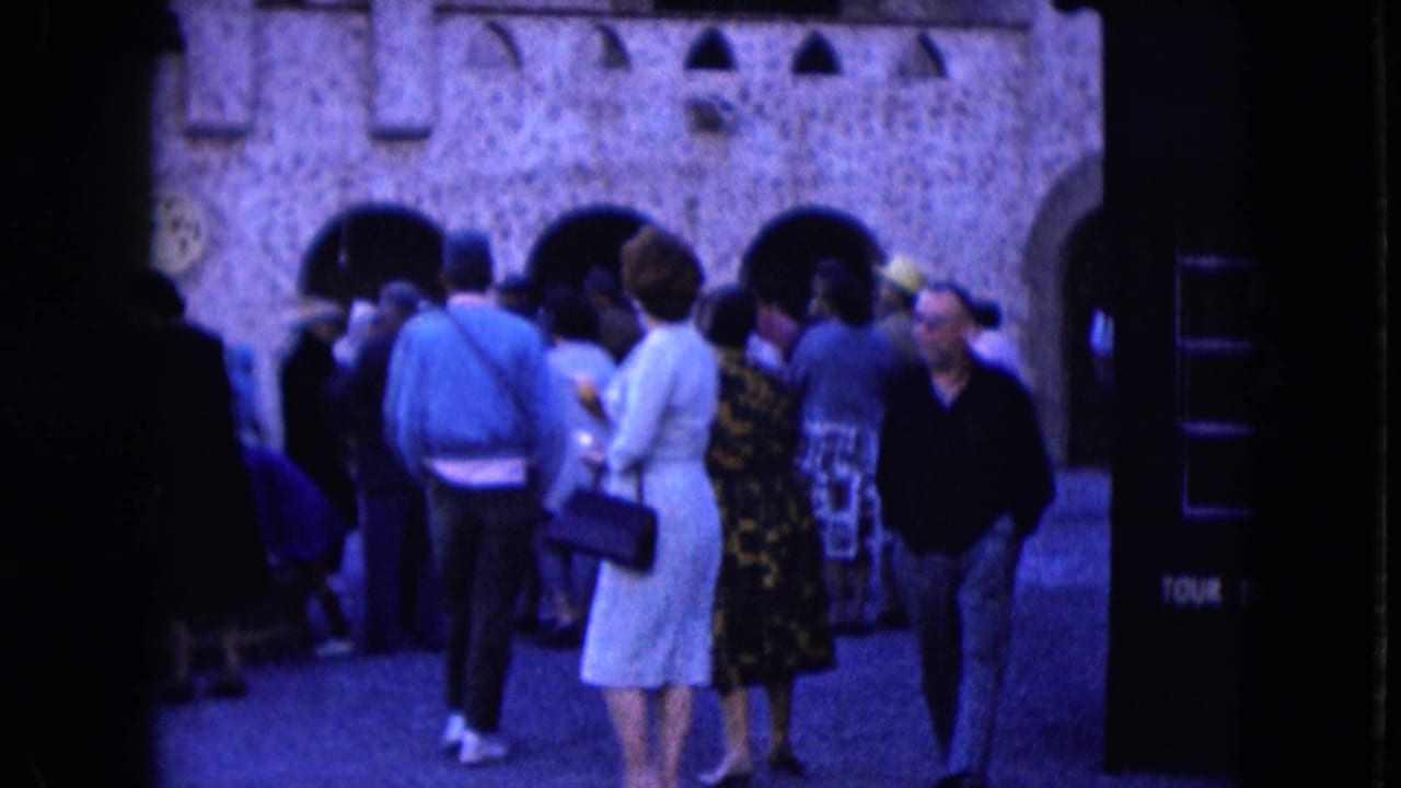 Crowd clusters in front of arched stone openings beside a tour ticket booth.